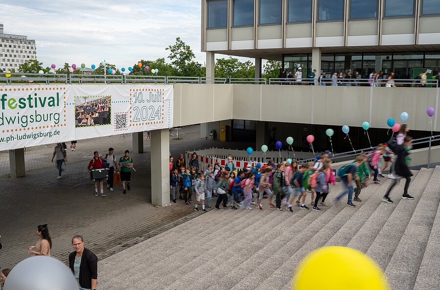 Kinder gehen die Stufen der mit Luftballons geschmückten Außentreppe der PH Ludwigsburg hoch.