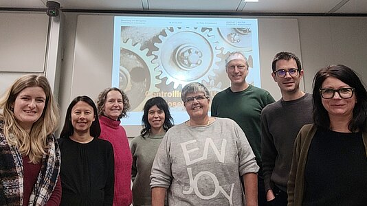 Dr. Petra Schneidewind und eine Gruppe Weiterbildungsteilnehmende stehen vor einer Projektion.