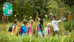 Auf dem Bild erkennt man eine Gruppe von Kindern mit ihrer Lehrerin in der Natur